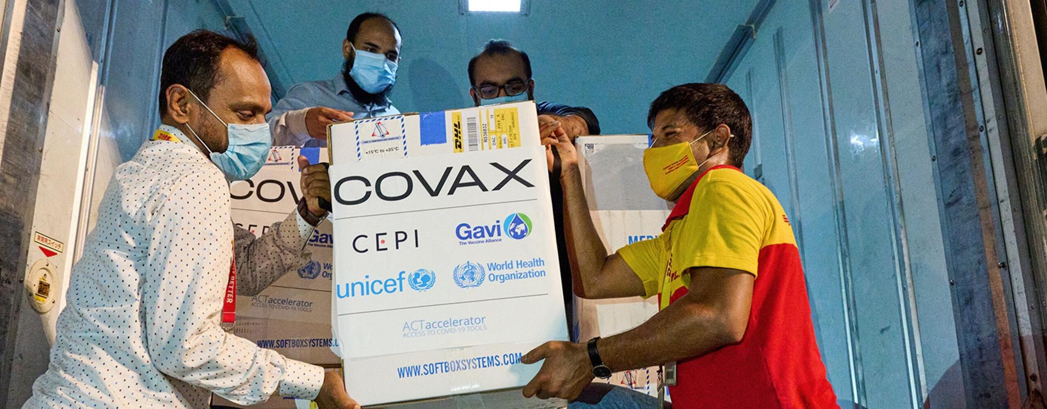 A group of men unload a box that says 'COVAX' from a truck.