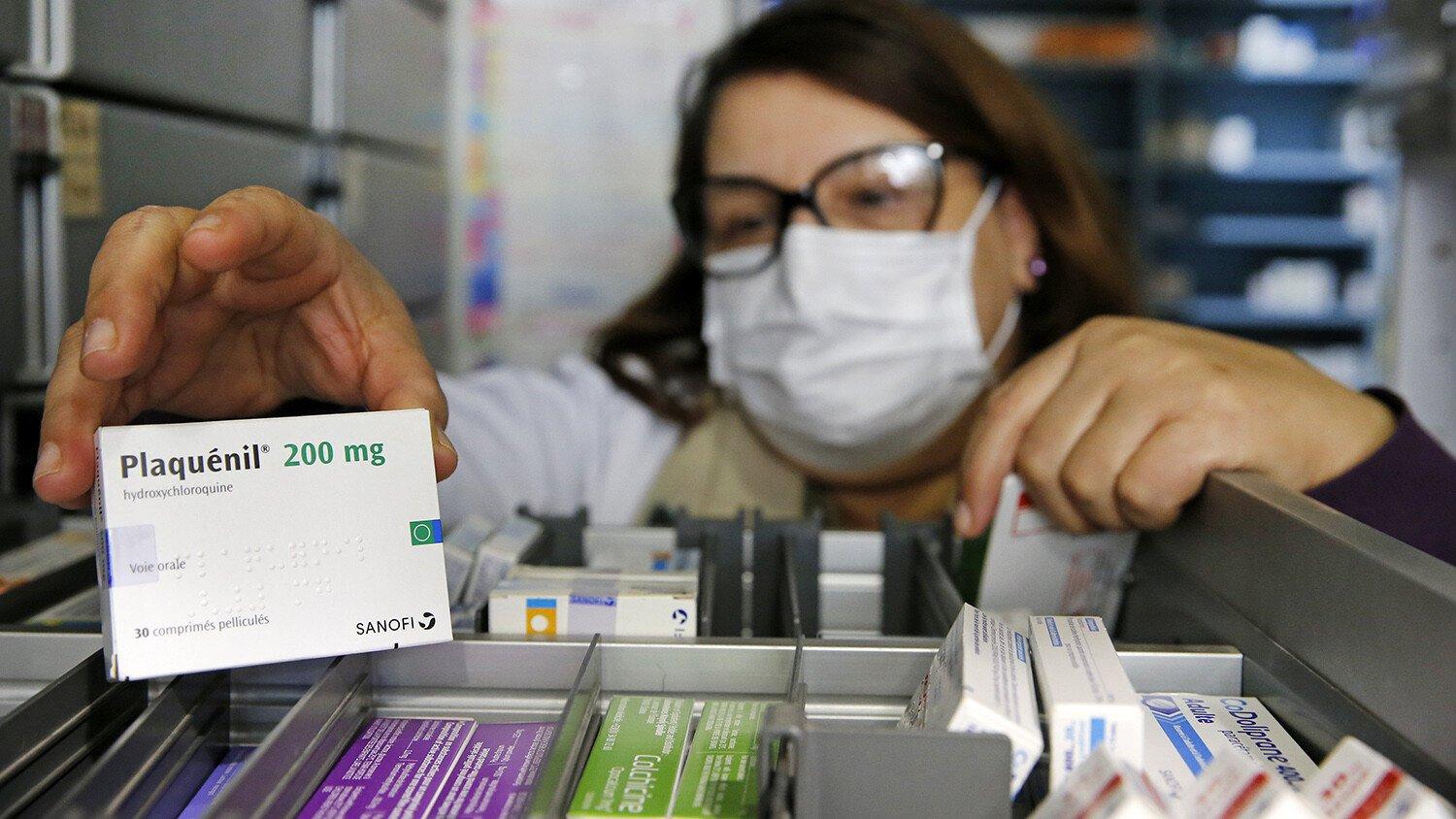 A pharmacy employee wearing a protective mask shows a box of Plaquenil (Chloroquine).