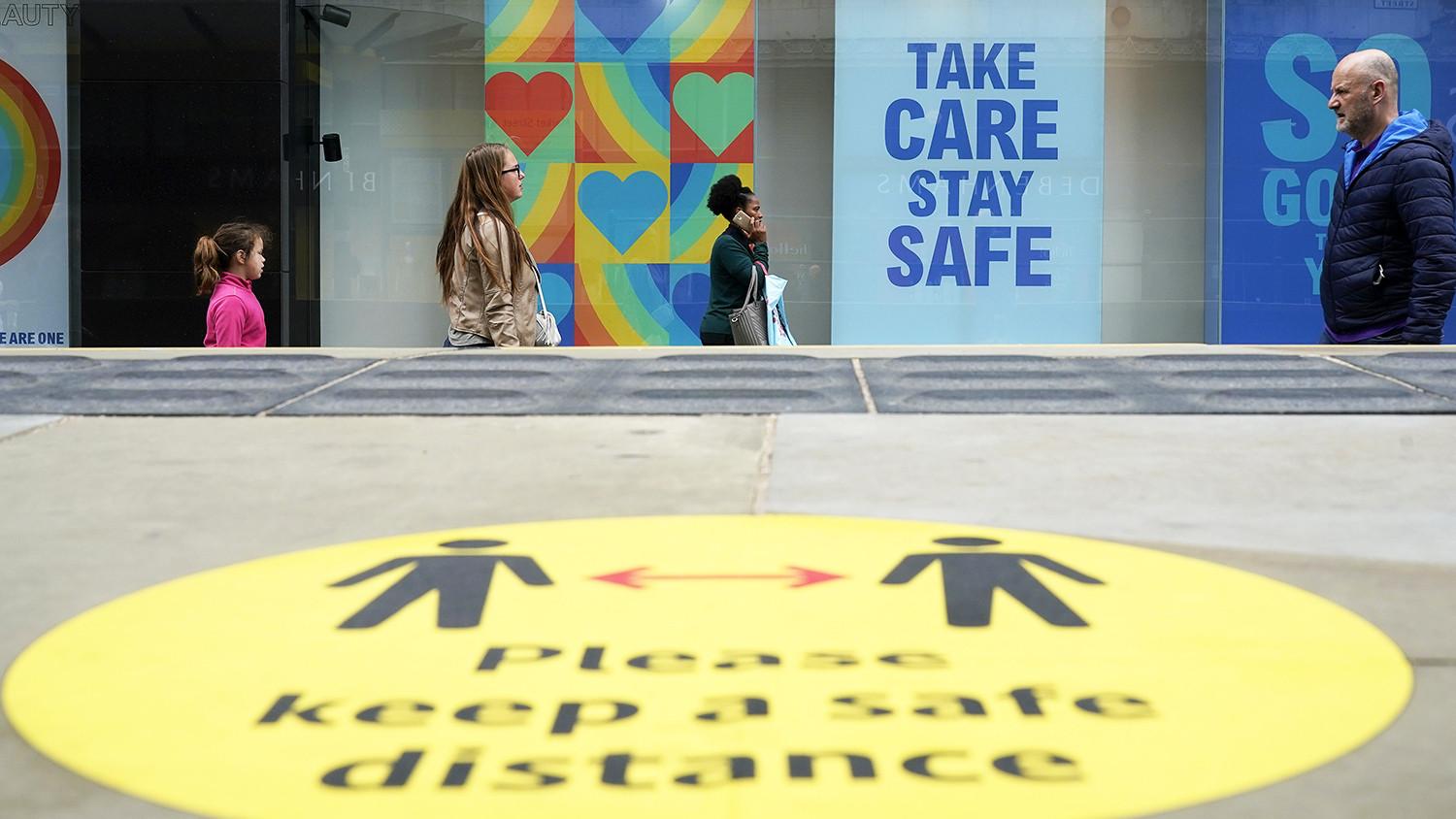 Shoppers walking on a street where coronavirus signs are visible.