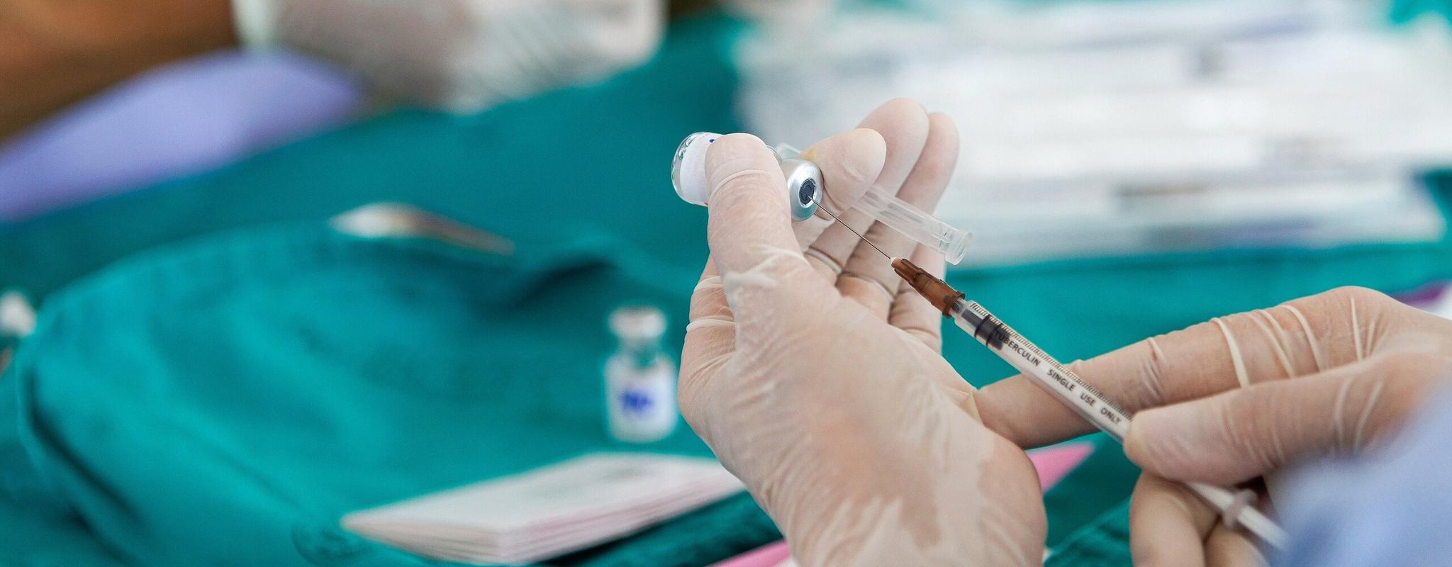 A pair of hands with surgical gloves poking an injection through a small bottle.