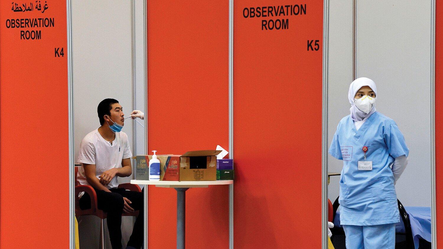 A nurse wearing a face mask and a vaccine trial volunteer sitting in an observation room in a repurposed convention centre in Manama, Bahrain. 