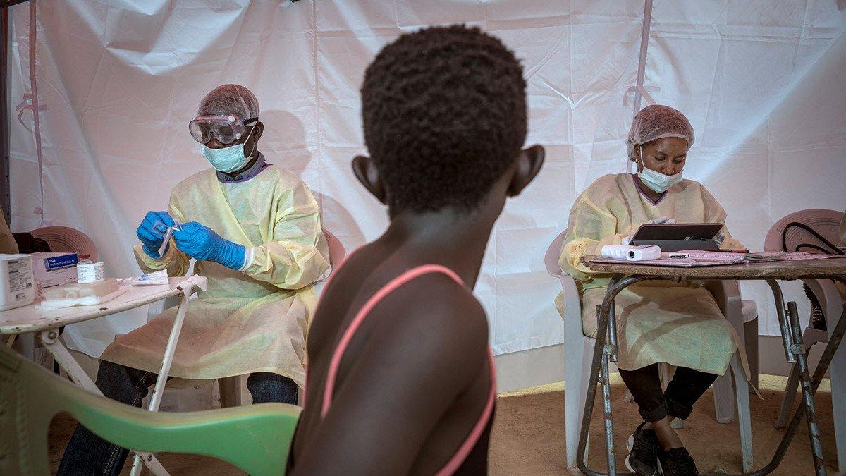 Young girl watches Ebola response team prepare vaccination equipment.