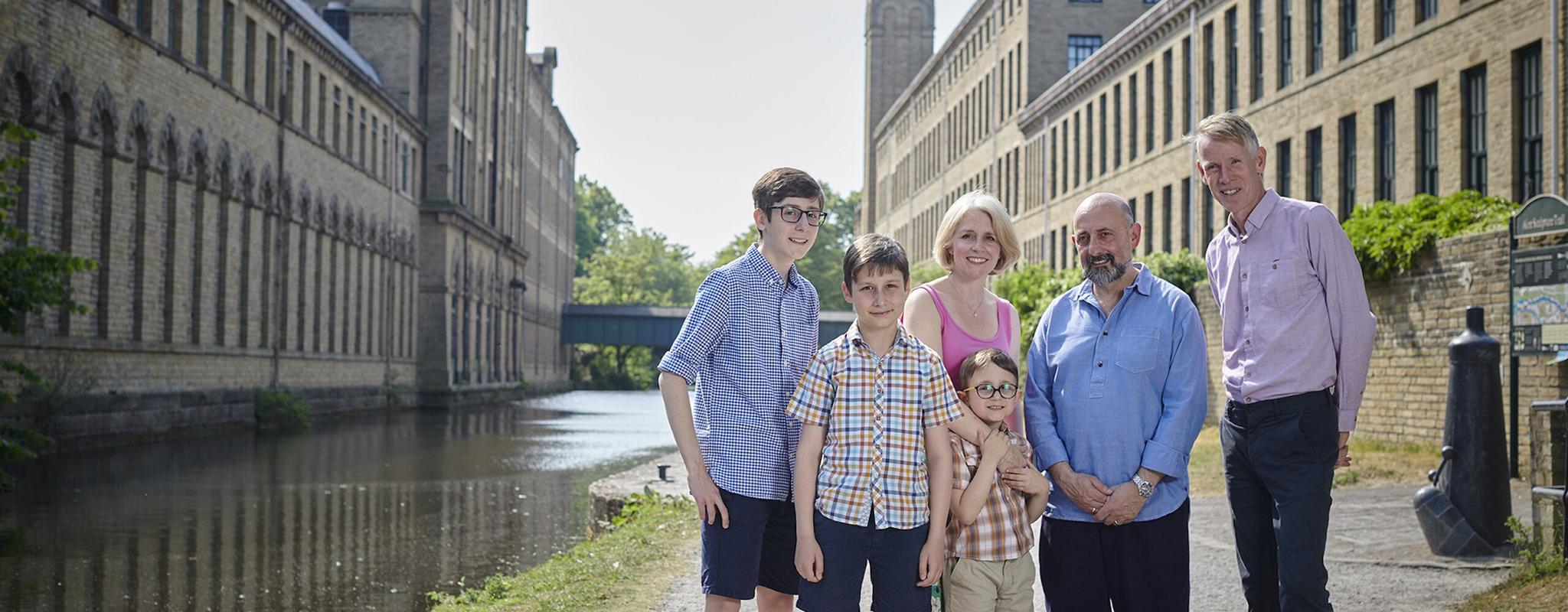 A group of five people, including three young boys, stand by the edge of a river in the city of Bradford.