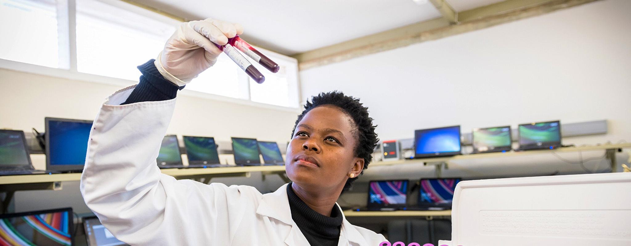 A woman holding a rack of blood samples (Image Ben Gilbert/Wellcome CC-BY)