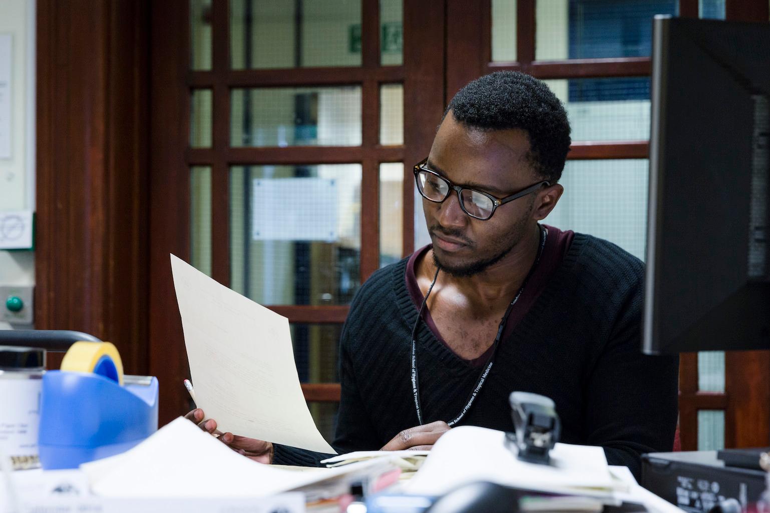 A researcher is sat as his desk reading through papers.