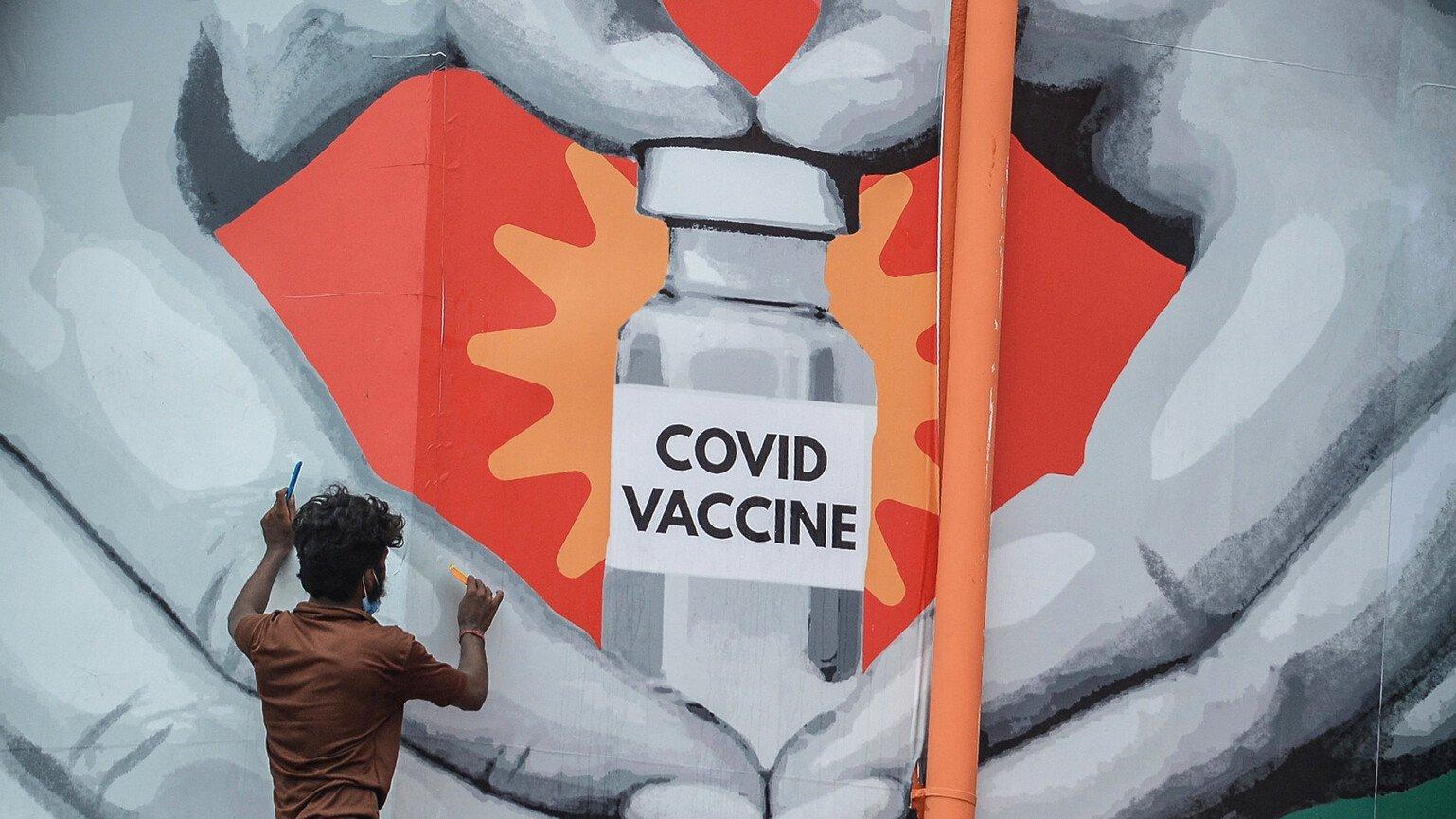 A man gives finishing touches to a huge mural that shows a Covid vaccine vile inside a heart hand. 