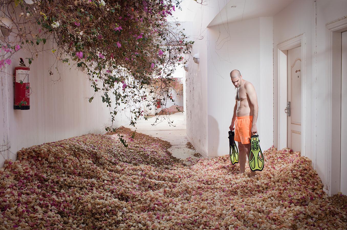 A man holding two flippers stands in a hotel room overgrown with rose bushes