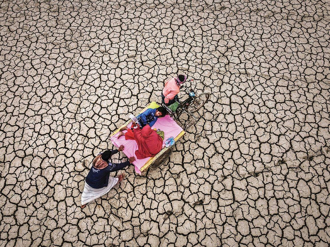 Parents carry their child on a stretcher across a desolate desert landscape.