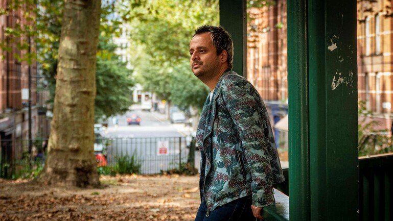 An image of a man wearing a leaf-patterned jacket. He is standing sideways, looking to the left.