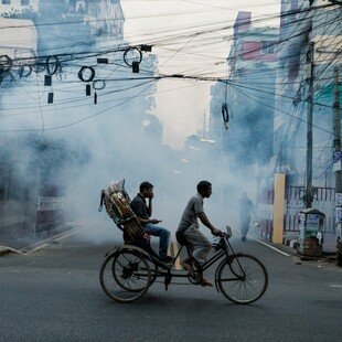 Two people cycling on a street in Uttara which is being sprayed with insecticide to kill mosquitoes