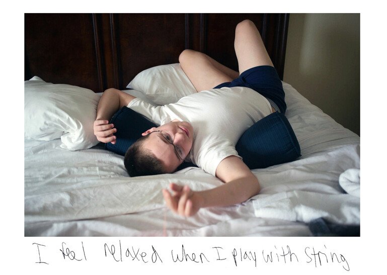 A 19-year-old man who is on the autistic spectrum lying on a bed playing with a piece of string