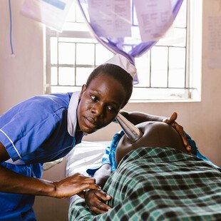 A midwife listens to the heartbeat of a fetus using a Pinard horn