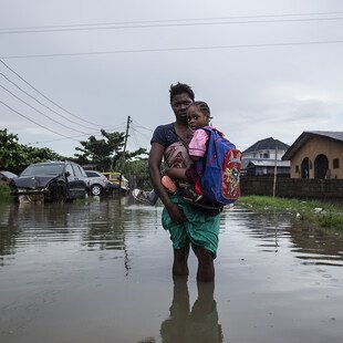 A mother carries her children to school through a flooded street