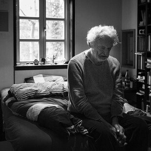 A man sits on the edge of his bed, in a sudden moment of confusion and distress