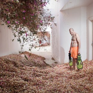 A man holding two flippers stands in a hotel room overgrown with rose bushes