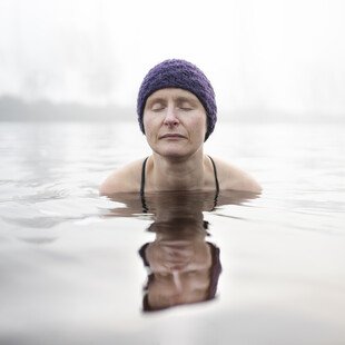 A woman wearing a swimming cap swims in cold water with her eyes closed