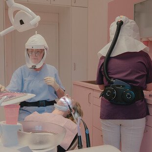 A dentist and patient both wear extensive PPE during a dental appointment.