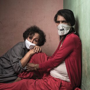 Two trans women sit on the ground, with one resting her head on the other's knee.