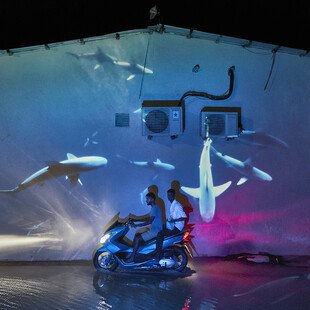 An underwater image is projected behind two men on a motorbike.