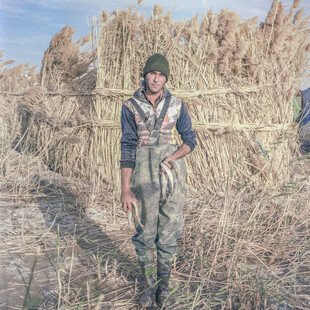 A young man stands holding a fish. 