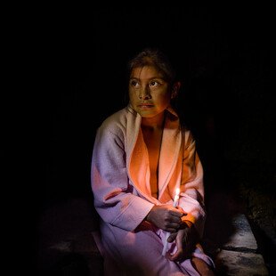 Petrona, age ten, sits on a wooden bench inside a chuj, a Mayan steam bath.