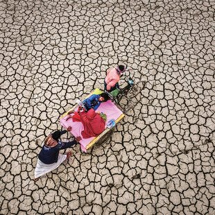 Parents carry their child on a stretcher across a desolate desert landscape.