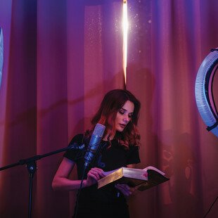 A woman records a video of herself reading a story in a soft-spoken voice.