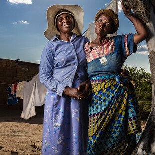 A counsellor and her patient stand outside a ruined house. 