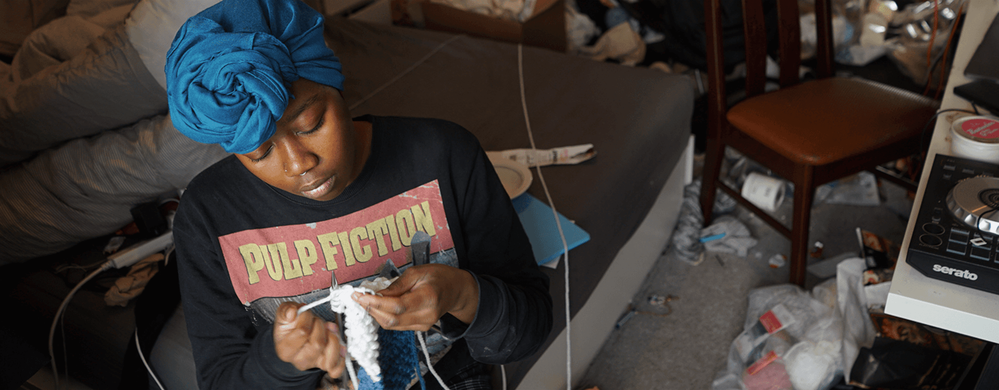 A woman sits in her bedroom during a lockdown, knitting. 